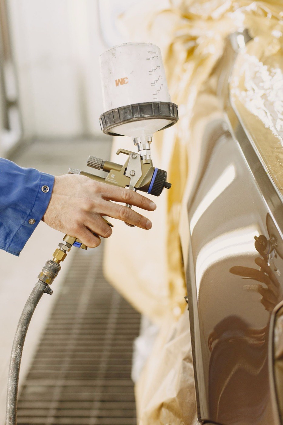 Profissional aplicando pintura automotiva com pistola em cabine de pintura